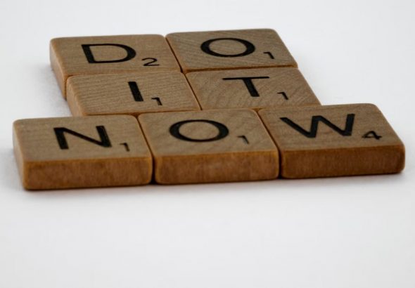 Wooden Scrabble tiles spelling 'Do It Now' on a white background. Motivational concept.
